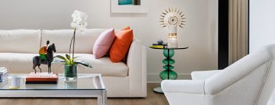 A modern sitting room in designer Seth Van Den Bergh’s studio with white furniture and colorful accents, including books, a sculpture, and an orchid on a glass table, painted Westhighland White by Sherwin-Williams.