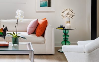 A modern sitting room in designer Seth Van Den Bergh’s studio with white furniture and colorful accents, including books, a sculpture, and an orchid on a glass table, painted Westhighland White by Sherwin-Williams.