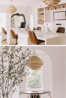 Modern office space with white desks and brown leather chairs, featuring iMac computers, large chandeliers, and built-in shelving.