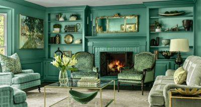 Luxurious living room with Surf Green walls and green decor, featuring a fireplace, armchairs, a sofa, a glass coffee table with flowers, and decorative shelves.