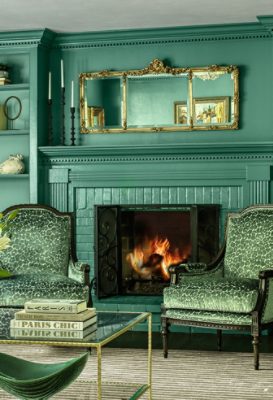 Luxurious living room with Surf Green walls and green decor, featuring a fireplace, armchairs, a sofa, a glass coffee table with flowers, and decorative shelves.