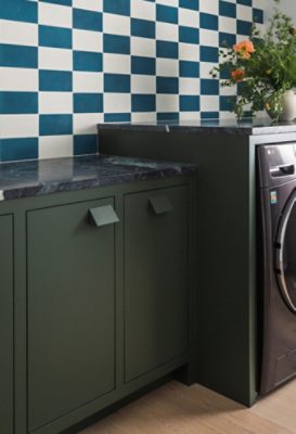 Modern laundry room with Jasper green cabinets, a checkered blue and white wall, and decorative items on the counter.