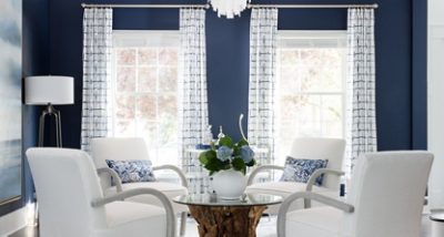 Modern living room with navy blue walls painted Distance by Sherwin-Williams, white armchairs, and blue hydrangeas on a wooden coffee table.