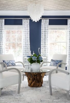 Modern living room with navy blue walls painted Distance by Sherwin-Williams, white armchairs, and blue hydrangeas on a wooden coffee table.