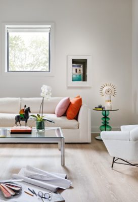 A modern sitting room in designer Seth Van Den Bergh’s studio with white furniture and colorful accents, including books, a sculpture, and an orchid on a glass table, painted Westhighland White by Sherwin-Williams.