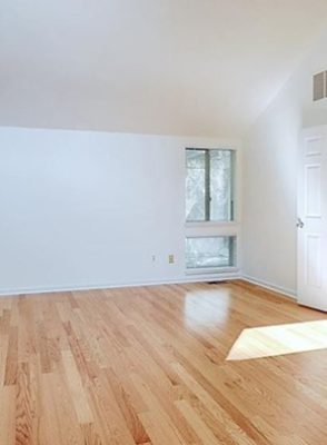 Empty room with white walls and hardwood floors, natural light.