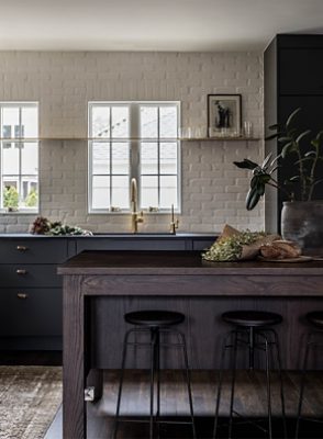 Image of modern kitchen with white brick walls, dark brown bartop, and dark green cabinets.