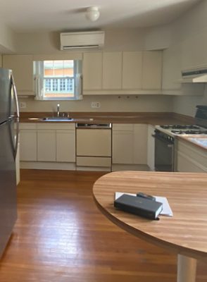 before photo of bland kitchen with white cabinets and wood accents.