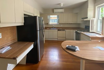 before photo of bland kitchen with white cabinets and wood accents.