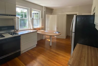 before photo of bland kitchen with white cabinets and wood accents.