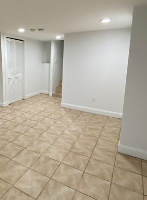 Empty room with white walls and tan tile floors.