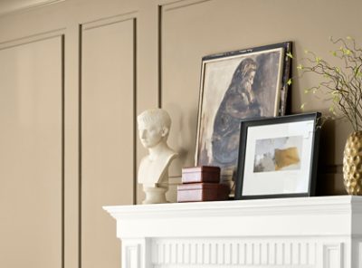 Decorative items on a white mantel against a paneled wall painted Universal Khaki, including a marble bust, artworks, and a gold vase with a branch. 