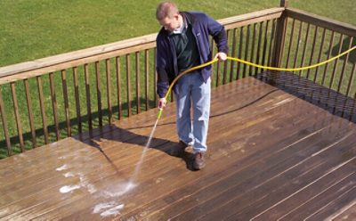A person cleaning a deck with a water hose.