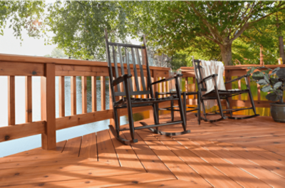 Black wooden rocking chairs on a cedar stained deck with a large tree next to a lake.