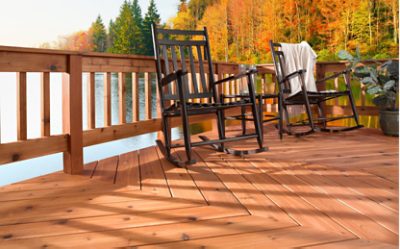 A deck stained a red-brown overlooking a lake with black wooden rocking chairs.
