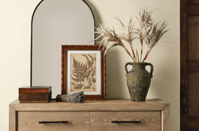 An accent table against a beige wall with an arched mirror.