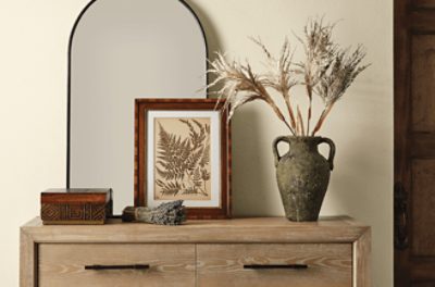 An accent table against a beige wall with an arched mirror.