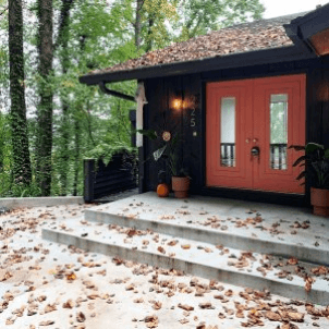 A front porch strewn with fallen leaves with orange painted French doors - photo by @kittystreehouse