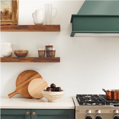 A kitchen with white walls with open, floating stained wood shelves and lower cabinets and range hood painted a gray-green.