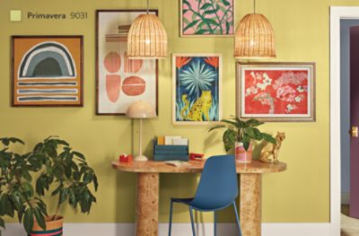 A gallery wall painted in SW 9031 Primavera with bright patterned art prints and an oval desk.