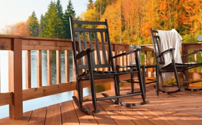 Wooden deck with black rocking chairs surrounding water and fall trees.