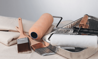 Painting supplies including brushes, rollers and paint trays resting on a drop cloth.