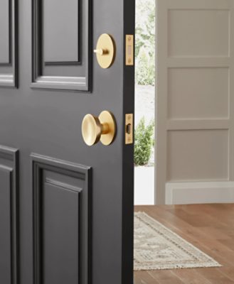 A foyer of a home with an open black door with a gold handle. Wooden floors with a rug and white walls.