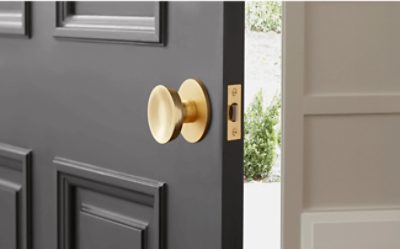 A foyer of a home with an open black door with a gold handle. Wooden floors with a rug and white walls.