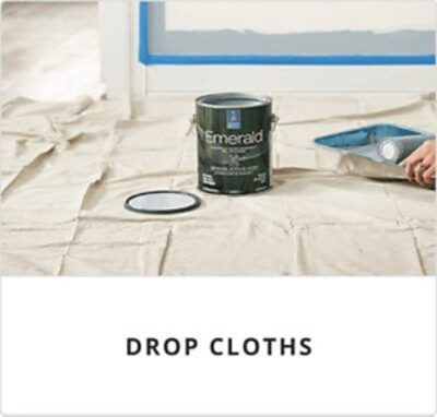 Drop cloths. A person rolling paint in a paint tray next to a can of Emerald on top of a drop cloth.