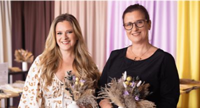 A photo of two people each holding a ceramic vase with dried wheat and flowers.