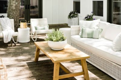 White wicker furniture on a wood deck with a light colored stained wood coffee table.