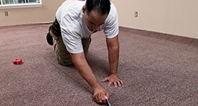 A person in an empty room using a knife to cut up carpet.