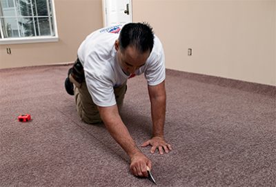 A person in an empty room using a knife to cut up carpet.