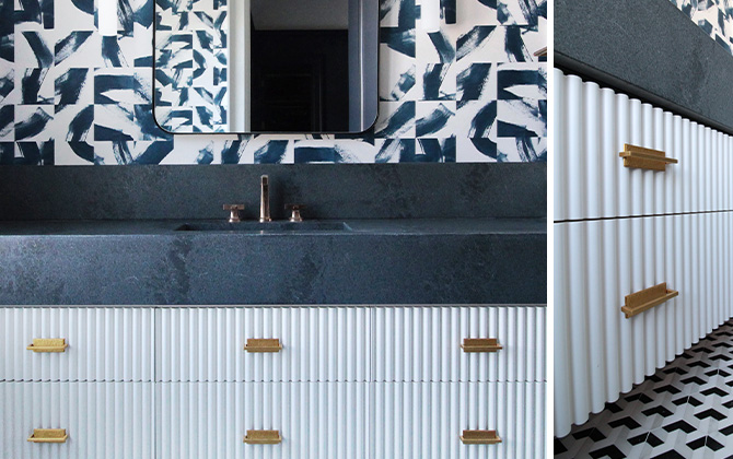 Full view and angled closeup of fluted white vanity with dark countertop and bold patterned wallpaper, dark blue tiled walk-in shower at right.