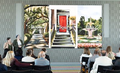 A group of people seated facing a projected image of three artworks displayed on a screen, representing the Roots, Soul, and Flair palettes of the Colors of Savannah project, with presenters standing nearby.