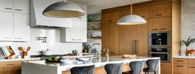 Modern kitchen with a white and wood theme, featuring a central island with bar stools and pendant lights.