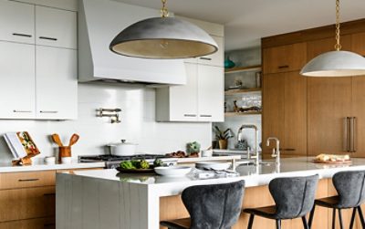 Modern kitchen with a white and wood theme, featuring a central island with bar stools and pendant lights.