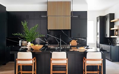 Modern kitchen with Tricorn Black cabinetry, Pure White ceiling, marble island, wooden barstools, and a vertical slatted hood.