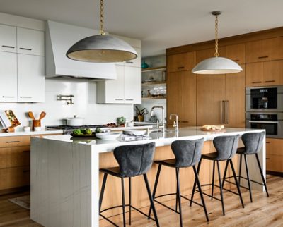 Modern kitchen with a white marble island, bar stools, pendant lights, and oak cabinetry. 