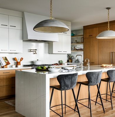 Modern kitchen with a white marble island, bar stools, pendant lights, and oak cabinetry. 