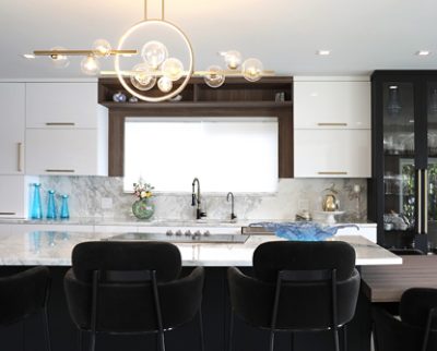 Modern kitchen with white cabinets, marble island, and chandelier. 