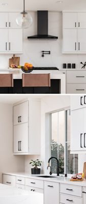 A modern kitchen with a central island, high-backed chairs, a range with black hood, light cabinets with black pulls, and a sink area with natural light. 