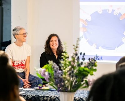 The Taste Curators smiling in front of a projected image, with flowers in the foreground. 