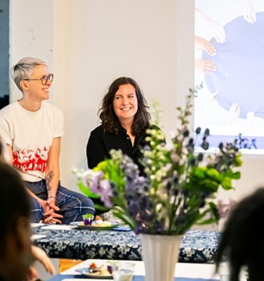 The Taste Curators smiling in front of a projected image, with flowers in the foreground. 