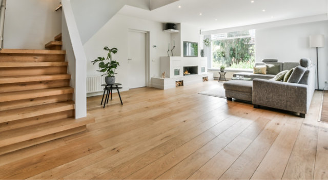 Modern living room with natural wood flooring, open staircase, and large windows showcasing a bright, contemporary interior.