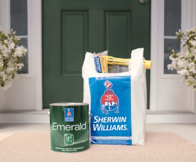 Una lata de Sherwin-Williams Emerald y una bolsa de suministros de pintura en la puerta de una casa.