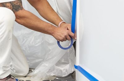 A painter placing FrogTape® Pro Grade Blue Painter's Tape on the bottom of door trim. trim