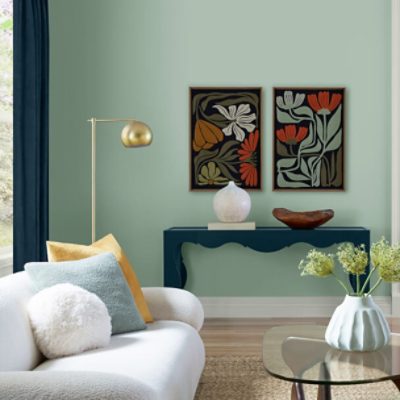 A living room with bold floral paintings hanging on a earthy green wall.