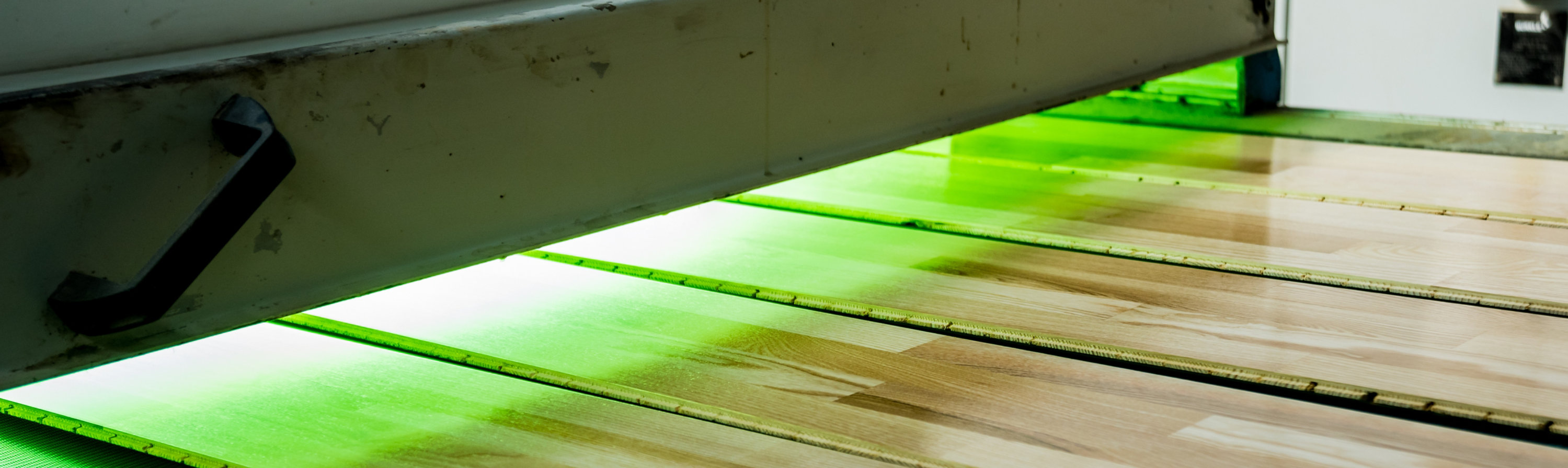 Wood flooring boards on a production line under UV curing lights, highlighting advanced coating technology and surface performance.