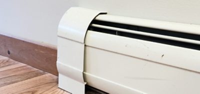 A white baseboard heater along a white wall with wood floors and baseboards.